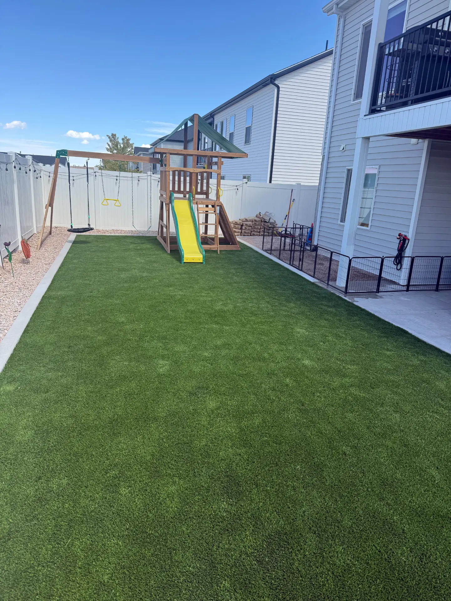 Backyard with fresh artificial turf, playground set and decorative rock borders